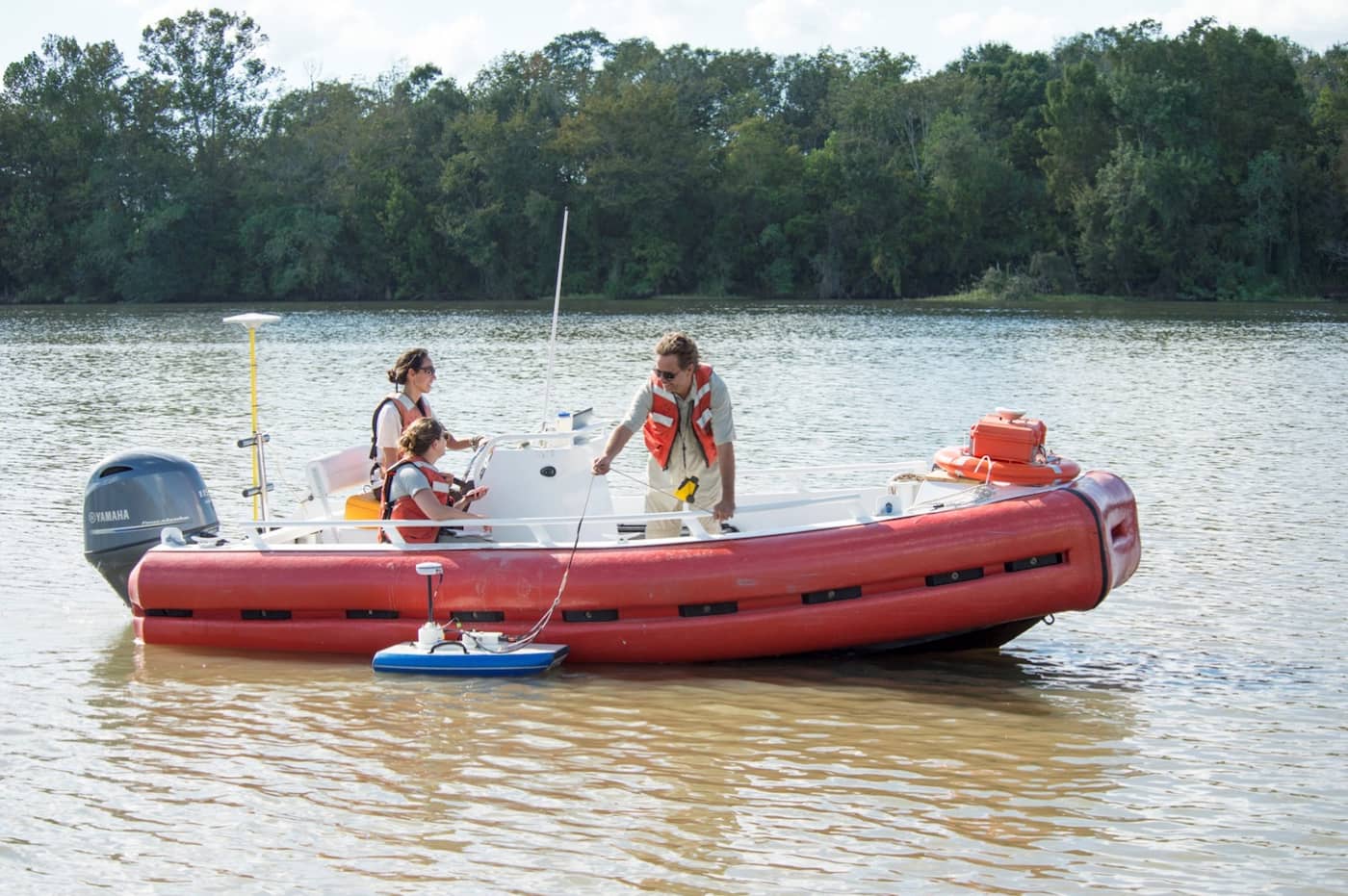 Two women and a man operate field instruments from inside an orange airboat